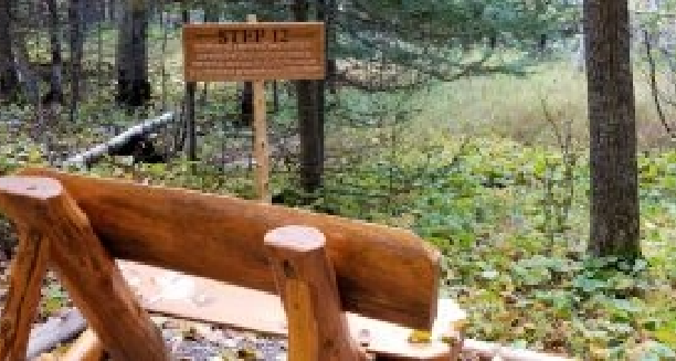 a wooden bench overlooking the woods and the Step 12 sign.
