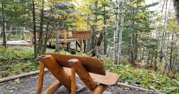 a wooden bench overlooking the woods and the Step 4 sign.