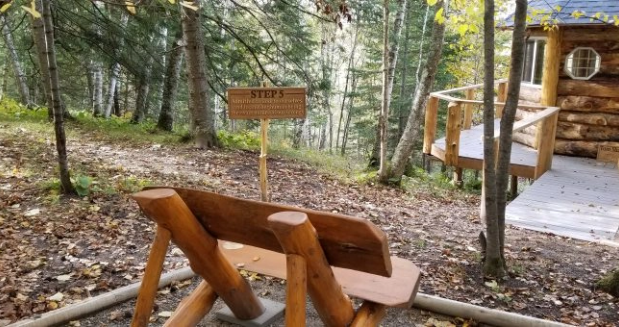 a wooden bench overlooking the woods and the Step 5 sign, near a log gazebo.