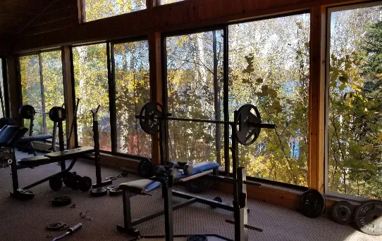 a fitness room with large windows and a great view of the woods and lake.