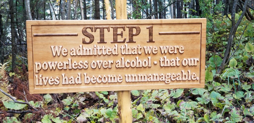 a carved wood sign that says "Step 1: We admitted that we were powerless over alcohol - that our lives had become unmanageable."